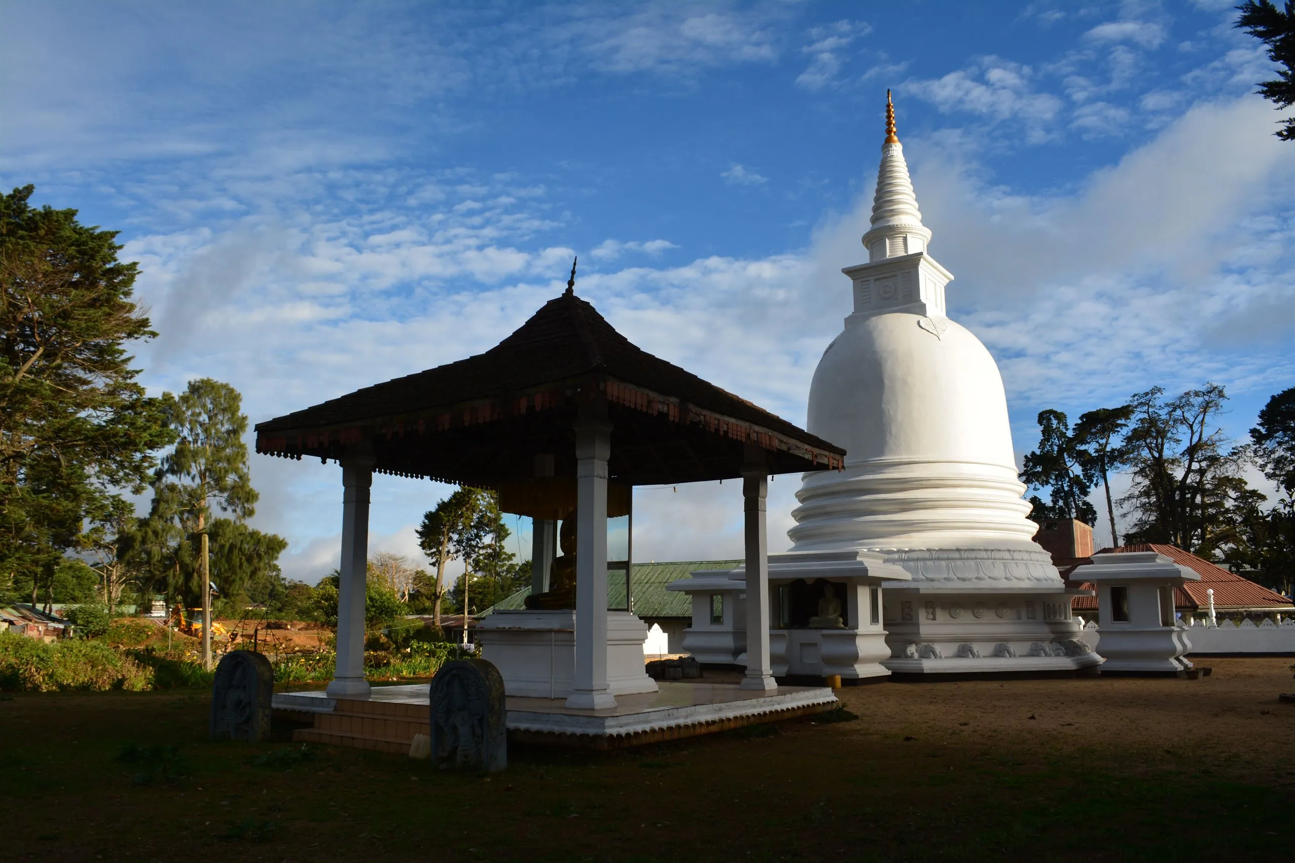Eine weiße Stupa und ein offener Pavillon mit goldenem Buddha an einem Tempel im Bergland