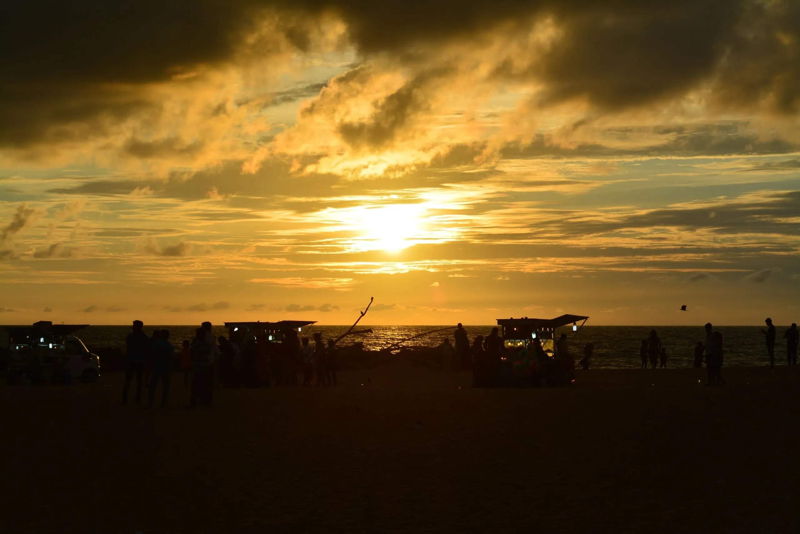 Sonnenuntergang über dem Meer am Strand von Negombo, Menschen und Essensstände als Silhouetten am Ufer