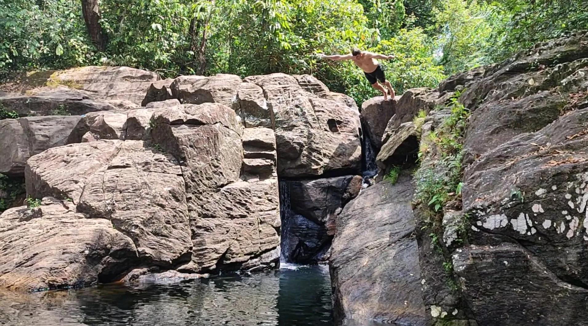Ein Gast springt von einem Felsvorsprung in das Becken unter dem Polgampola-Wasserfall