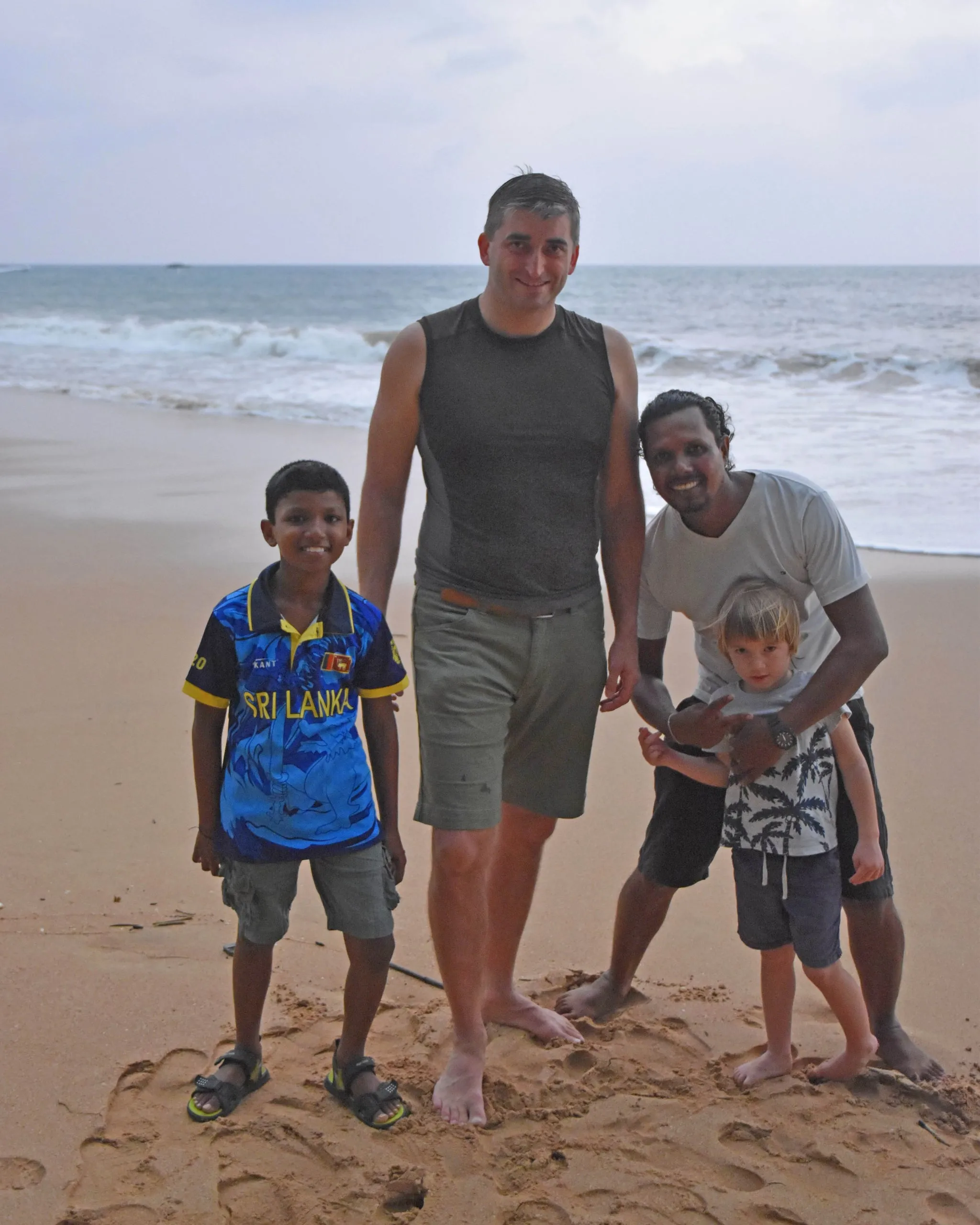 Ein großer Besucher und ein Guide stehen in der Dämmerung am Strand mit zwei Jungen, einem aus Sri Lanka und einem aus Tschechien