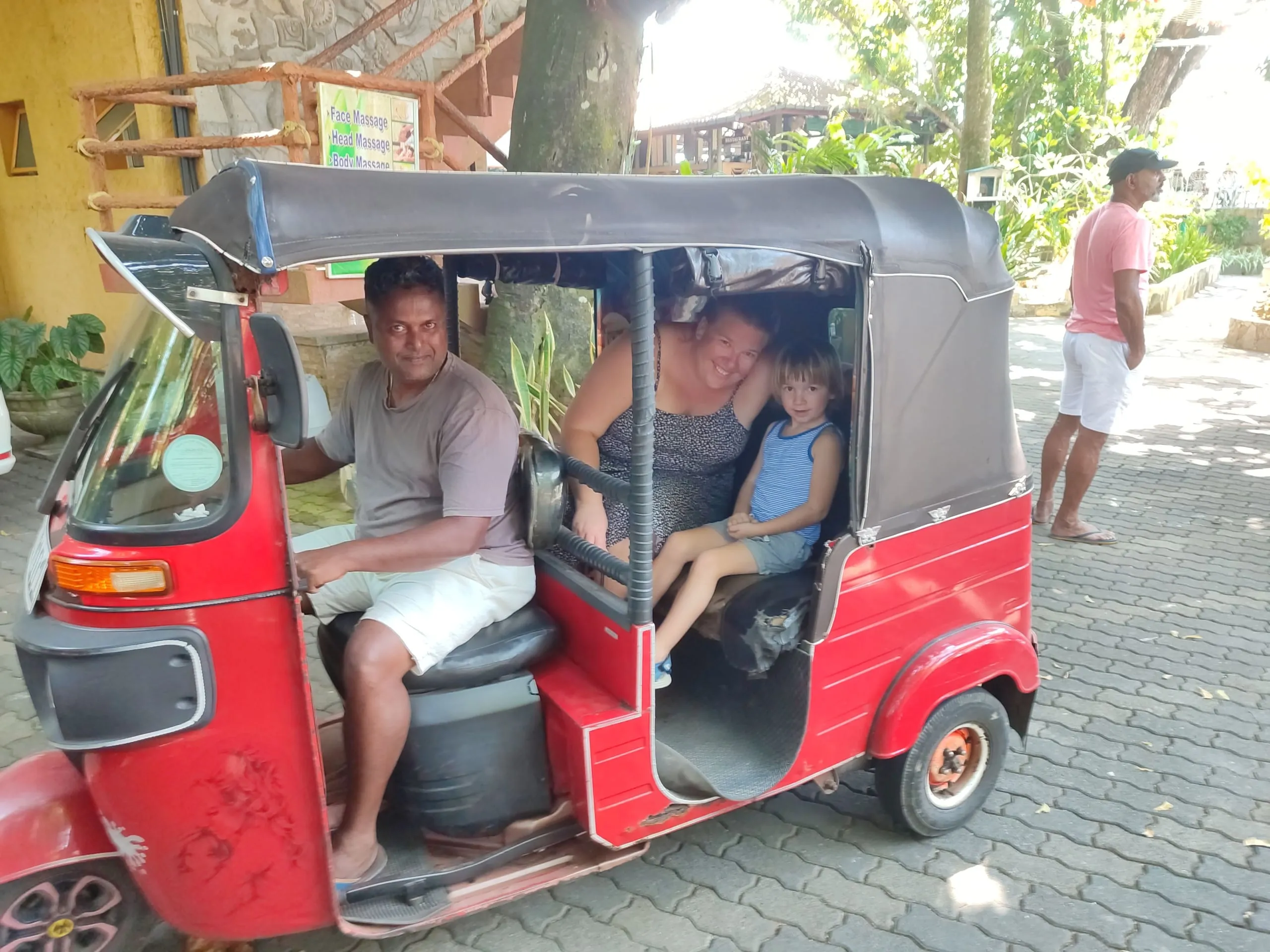 Eine Frau und ein kleiner Junge sitzen hinten in einem roten Tuk-Tuk, der Fahrer am Lenker