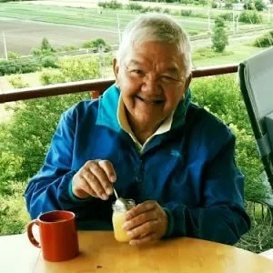 Tony Achmat smiling at a table outdoors, green fields behind him